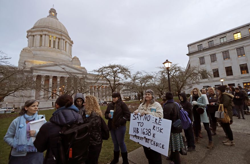 Kebby Johnson, center, of Spokane, Wash., holds a sign that reads "Say No to HB 1638," as she waits in line, Friday, Feb. 8, 2019, to attend a public hearing before the House Health Care & Wellness Committee at the Capitol in Olympia, Wash. Amid a measles outbreak that has sickened people in Washington state and Oregon, lawmakers heard public testimony Friday on a bill that would remove parents' ability to claim a philosophical exemption to opt their school-age children out of the combined measles, mumps and rubella vaccine. (AP Photo/Ted S. Warren)