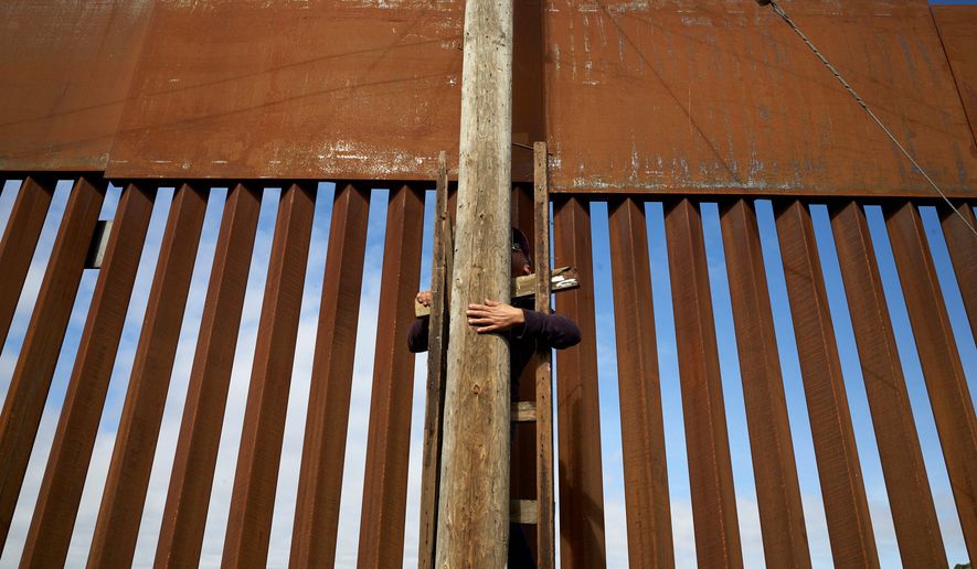 In this Jan. 16, 2019, image, a man uses a ladder to climb an electrical pole in a border neighborhood in Tijuana, Mexico, alongside a newly-replaced section of the border wall. The U.S. faces a delicate dance as it charts a course to extend or replace border barriers near homes and structures. (AP Photo/Gregory Bull)