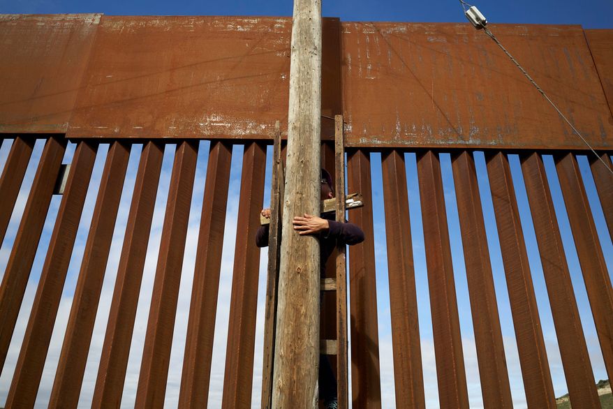 In this Jan. 16, 2019, image, a man uses a ladder to climb an electrical pole in a border neighborhood in Tijuana, Mexico, alongside a newly-replaced section of the border wall. The U.S. faces a delicate dance as it charts a course to extend or replace border barriers near homes and structures. (AP Photo/Gregory Bull)