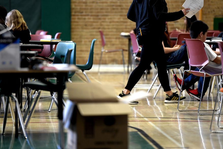 A teacher moves from table-to-table while teaching one of two combined sixth-grade classes in the gymnasium at Skinner Middle School during the first day of the Denver Public Schools teachers strike, Monday, Feb. 11, 2019, in Denver. More negotiations are set for Tuesday. (Joe Amon/The Denver Post via AP)