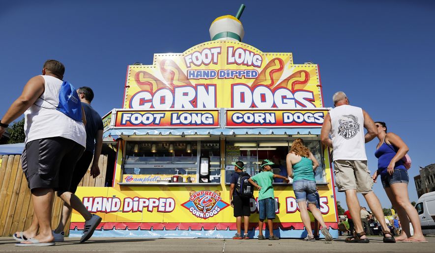 FILE - In this Aug. 9, 2018 file photo, Iowa State fairgoers line up to get a corn dog at a concession stand during the opening day of the Iowa State Fair in Des Moines, Iowa. The Iowa State Fair has confirmed that it will require all food and drink vendors to accept credit and debit card payments beginning in 2020. Cash has long been the dominant method of payment for the fried cheese curds, corn dogs, and scores of other foods bought by fairgoers. (AP Photo/Charlie Neibergall, File)