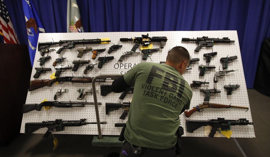 An FBI agent displays seized firearms before a news conference Wednesday, Feb. 13, 2019, in Los Angeles. Federal prosecutors say they've dealt a blow to two Los Angeles gangs that have ties to the Mexican Mafia after charging dozens of suspected members with racketeering and drug and gun violations. (AP Photo/Jae C. Hong)