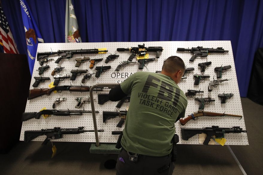 An FBI agent displays seized firearms before a news conference Wednesday, Feb. 13, 2019, in Los Angeles. Federal prosecutors say they've dealt a blow to two Los Angeles gangs that have ties to the Mexican Mafia after charging dozens of suspected members with racketeering and drug and gun violations. (AP Photo/Jae C. Hong)