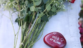 Flowers and stones are shown at a memorial outside Marjory Stoneman Douglas High School during the one-year anniversary of the school shooting, Thursday, Feb. 14, 2019, in Parkland, Fla.  A year ago on Thursday, 14 students and three staff members were killed when a gunman opened fire at the high school.  (AP Photo/Wilfredo Lee)