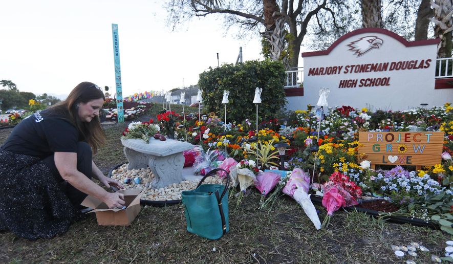 Suzanne Devine Clark, an art teacher at Deerfield Beach Elementary School, places painted stones at a memorial outside Marjory Stoneman Douglas High School during the one-year anniversary of the school shooting, Thursday, Feb. 14, 2019, in Parkland, Fla. A year ago on Thursday, 14 students and three staff members were killed when a gunman opened fire at the high school.  (AP Photo/Wilfredo Lee)