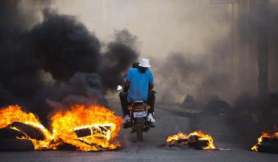 People on a motorcycle drive past a burning roadblock placed by anti-government protesters who are demanding the resignation of Haitian President Jovenel Moise, near the presidential palace in Port-au-Prince, Haiti, Wednesday, Feb. 13, 2019. (AP Photo/Dieu Nalio Chery)