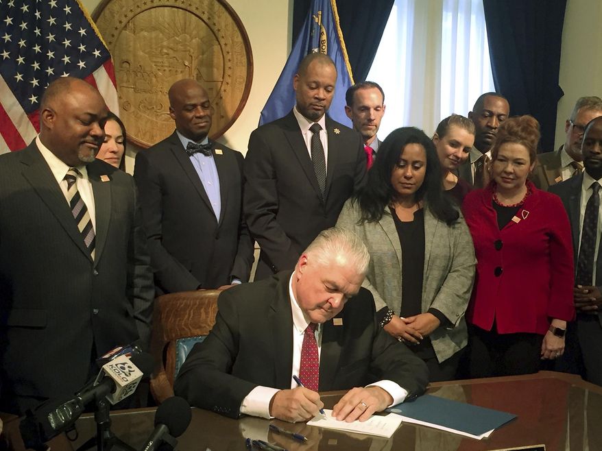 Nevada Gov. Steve Sisolak surrounded by lawmakers who supported gun control, signs legislation expanding background checks to private gun sales and transfers in Carson City, Nev., Friday, Feb. 15, 2019. Gov. Sisolak signed into law a measure closing a loophole that allows gun buyers to avoid background checks by going through unlicensed gun sellers. The bill came shortly after the state Assembly approved the measure. (AP Photo/Ryan Tarinelli)