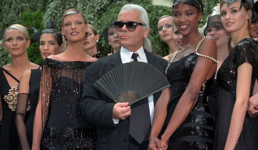 FILE - In this Tuesday July 9, 1996 file photo, Karl Lagerfeld is surrounded by Canadian model Linda Evangelista, left, and British model Naomi Campbell, right, and other models after the presentation of his 1996-97 fall-winter haute couture fashion collection for Chanel in Paris. Chanel's iconic couturier, Karl Lagerfeld, whose accomplished designs as well as trademark white ponytail, high starched collars and dark enigmatic glasses dominated high fashion for the last 50 years, has died. He was around 85 years old. (AP Photo/Lionel Cironneau, File)