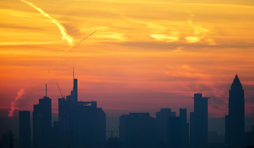 A plane flies over the banking district during sunrise in Frankfurt, Germany, Saturday, Feb. 16, 2019. (AP Photo/Michael Probst)