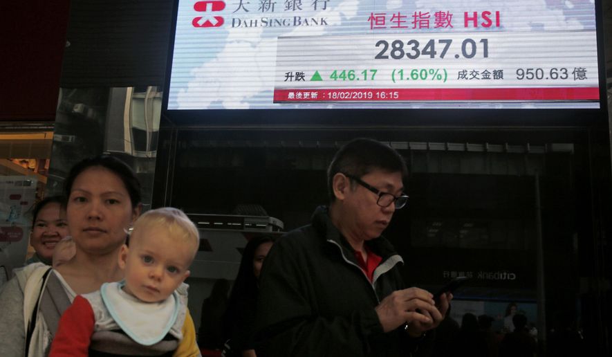 People walk past an electronic board showing Hong Kong share index outside a bank in Hong Kong, Wednesday, Feb. 20, 2019. Shares were mostly higher in Asia on Wednesday after a modestly high finish on Wall Street that extended the market’s gains into a fourth week.(AP Photo/Kin Cheung)