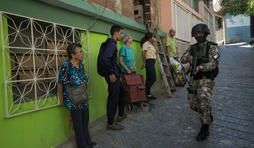 Residents stand near a wall as they watch a member of the National Police Action Force, or FAES, an elite commando unit created for anti-gang operations, patrol the Antimano neighborhood of Caracas, Venezuela, Tuesday, Jan. 29, 2019. Human Rights Watch has detailed widespread abuses by members of Venezuela's security forces in reports published in 2014 and 2017. (AP Photo/Rodrigo Abd)