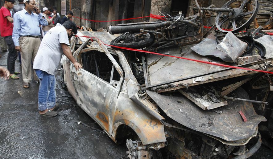 People look at a charred vehicle in Dhaka, Bangladesh, Friday, Feb. 22, 2019. Police on Friday were seeking up to a dozen suspects in connection with a fire in the oldest part of Bangladesh's capital that killed scores of people. (AP Photo/Mahmud Hossain Opu )
