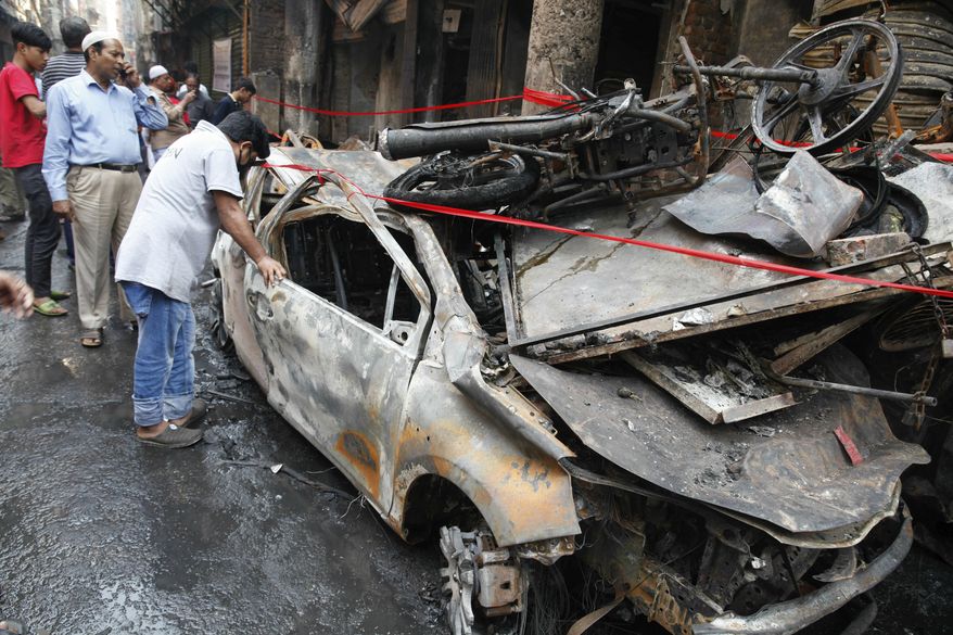 People look at a charred vehicle in Dhaka, Bangladesh, Friday, Feb. 22, 2019. Police on Friday were seeking up to a dozen suspects in connection with a fire in the oldest part of Bangladesh's capital that killed scores of people. (AP Photo/Mahmud Hossain Opu )