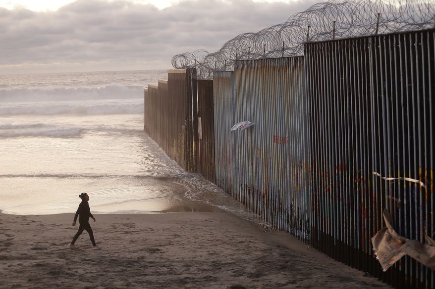 FILE - In this Jan. 9, 2019 file photo, a woman walks on the beach next to the border wall topped with razor wire in Tijuana, Mexico. A group of former U.S. national security officials is set to release a statement on Monday, Feb. 25, arguing that there is no justification for President Donald Trump to use a national emergency declaration to fund a wall along the U.S.-Mexico border. (AP Photo/Gregory Bull, File)