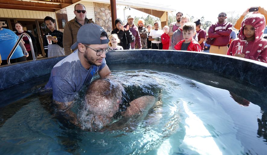 Church members watch as student pastor Craig Blaylock, left, baptizes Blake Brown, at the First Pentecostal Church in Columbus, Miss., Sunday morning, Feb. 24, 2019. The church, in the background, was destroyed by a tornado Saturday afternoon, but church members opted to go ahead with the baptisms as planned. (AP Photo/Rogelio V. Solis)