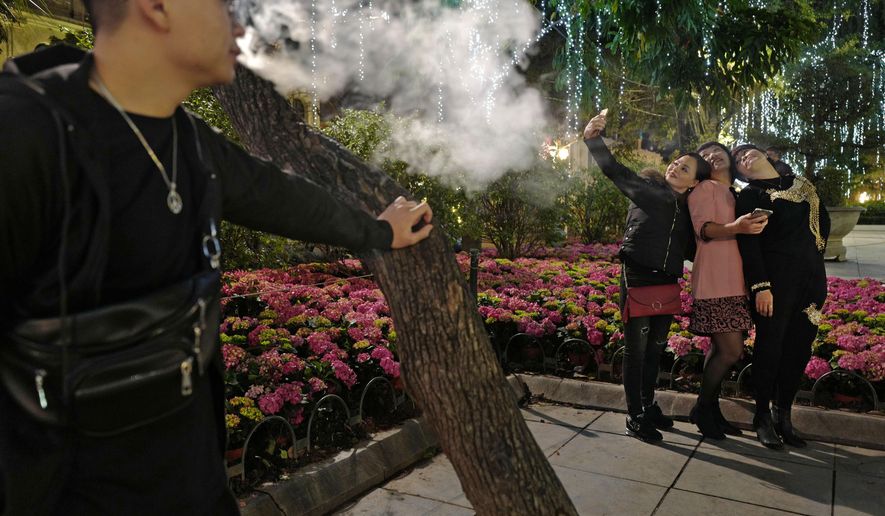 In this Saturday, Feb. 23, 2019, photo, women pose for a selfie while a man smokes at a peak near Hoan Kiem Lake in Hanoi, Vietnam. As Vietnam’s capital gears up for the second summit between U.S. President Donald Trump and North Korean leader Kim Jong Un, people take time to relax at nighttime by Hoan Kiem Lake in downtown Hanoi. (AP Photo/Vincent Yu)