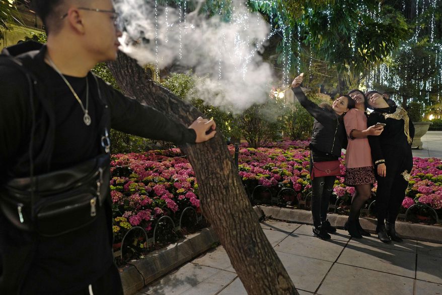 In this Saturday, Feb. 23, 2019, photo, women pose for a selfie while a man smokes at a peak near Hoan Kiem Lake in Hanoi, Vietnam. As Vietnam’s capital gears up for the second summit between U.S. President Donald Trump and North Korean leader Kim Jong Un, people take time to relax at nighttime by Hoan Kiem Lake in downtown Hanoi. (AP Photo/Vincent Yu)