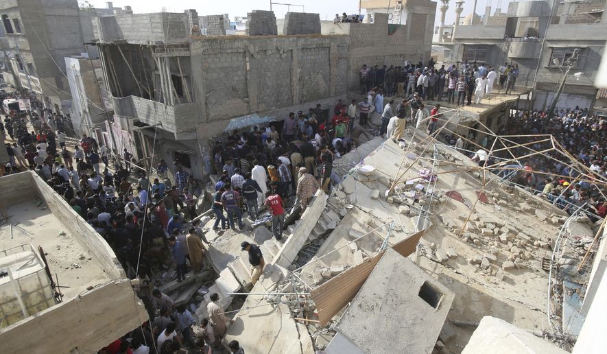 People gather near a collapsed building while rescue work is in progress in Karachi, Pakistan, Monday, Feb. 25, 2019. The small residential building collapsed as construction work was underway next to it in the city's Malir neighborhood. (AP Photo/Fareed Khan)