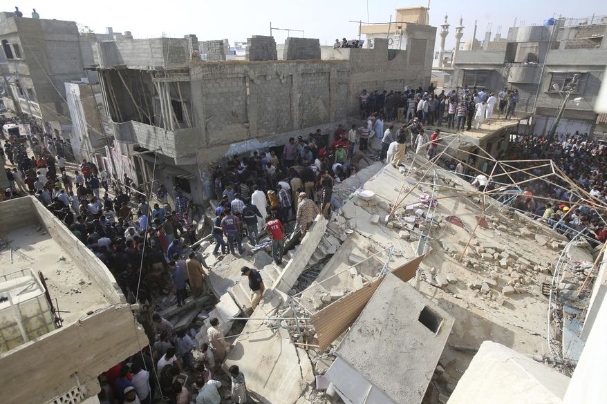 People gather near a collapsed building while rescue work is in progress in Karachi, Pakistan, Monday, Feb. 25, 2019. The small residential building collapsed as construction work was underway next to it in the city's Malir neighborhood. (AP Photo/Fareed Khan)