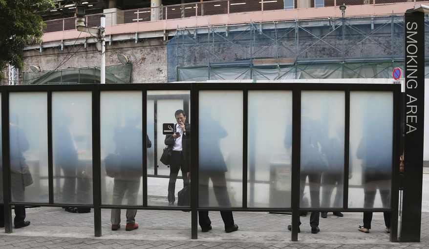 FILE - In this April 7, 2017, file photo, people gather at a smoking area in Tokyo. Tokyo is a smokers’ heaven. Despite tougher laws enacted last year, smokers can still light up in small restaurants and bars. Tobacco advertising is allowed on television, cigarette packages don’t contain graphic health warnings, and tobacco is cheap compared to prices in other world cities. Tokyo organizers on Thursday, Feb. 28, 2019, announced a stringent ban on all tobacco products and vaping devices. Smoking will be banned at any indoor or outdoor Olympic or Paralympic venue _ including perimeter areas being run Tokyo 2020. (AP Photo/Koji Sasahara, File)