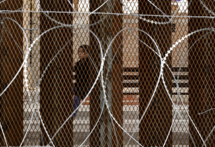 A woman waiting for a bus in Nogales, Mexico, is framed by a razor-wire-covered border wall separating it from Nogales, Ariz., Saturday, March 2, 2019. (AP Photo/Charlie Riedel)