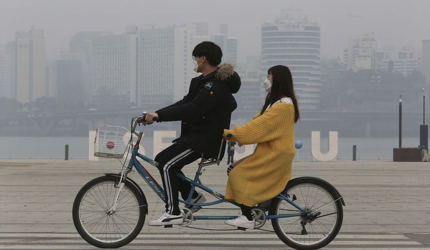 A couple wearing masks ride a bicycle as the cityscape is covered with a thick haze of fine dust particles in Seoul, South Korea, Tuesday, March 5, 2019. South Korean Environment Ministry issued emergency fine dust reduction measures on Tuesday. (AP Photo/Ahn Young-joon)