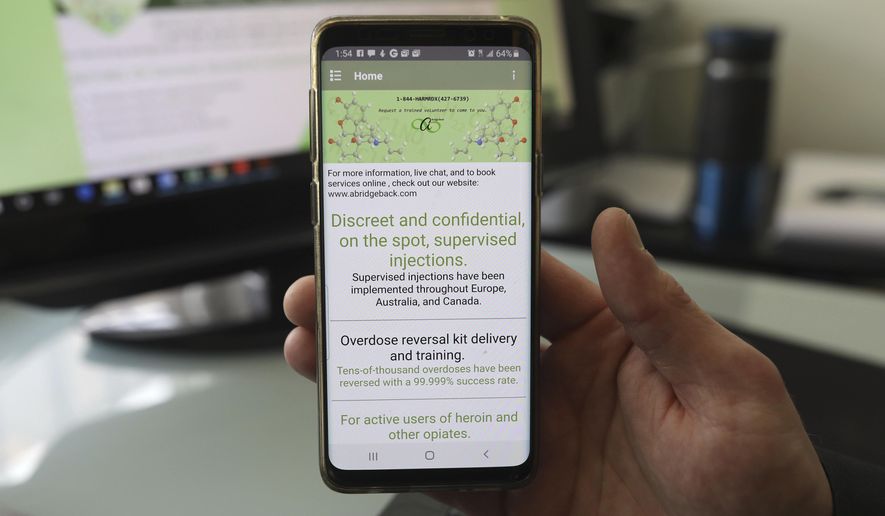 This Feb. 21, 2019 photo shows Lucien Izraylov, an addiction counselor and former heroin user, holds his phone with an open app he created in his office in Evanston, Ill. The smartphone app is design to connect drug users with volunteers who will make sure they don't overdose. (Abel Uribe/Chicago Tribune via AP)
