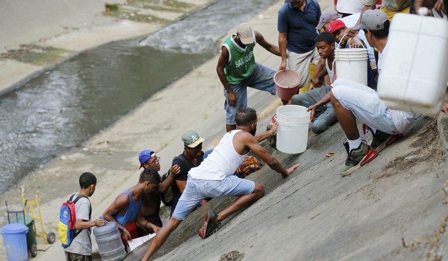 People collect water falling from a leaking pipeline on the bank of the Guaire River during rolling blackouts, which affects access to running water, in Caracas, Venezuela, Monday, March 11, 2019. The blackout has intensified the toxic political climate, with opposition leader Juan Guaido blaming alleged government corruption and mismanagement and President Nicolas Maduro accusing his U.S.-backed adversary of sabotaging the national grid. (AP Photo/Fernando Llano)