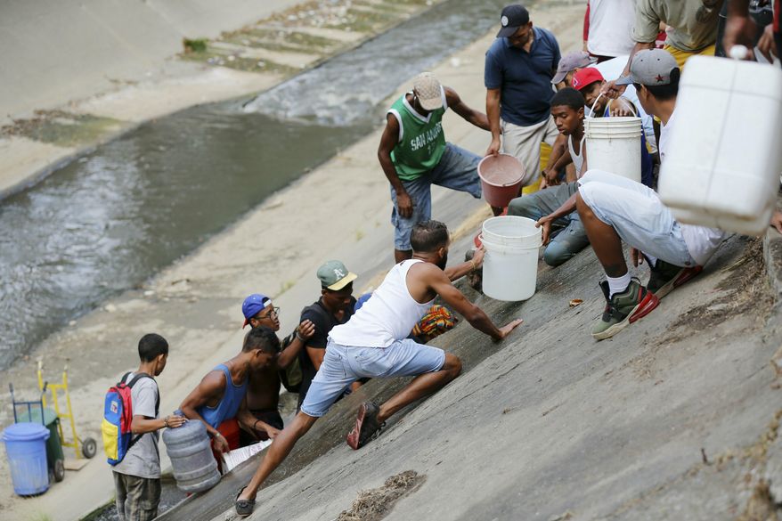 People collect water falling from a leaking pipeline on the bank of the Guaire River during rolling blackouts, which affects access to running water, in Caracas, Venezuela, Monday, March 11, 2019. The blackout has intensified the toxic political climate, with opposition leader Juan Guaido blaming alleged government corruption and mismanagement and President Nicolas Maduro accusing his U.S.-backed adversary of sabotaging the national grid. (AP Photo/Fernando Llano)
