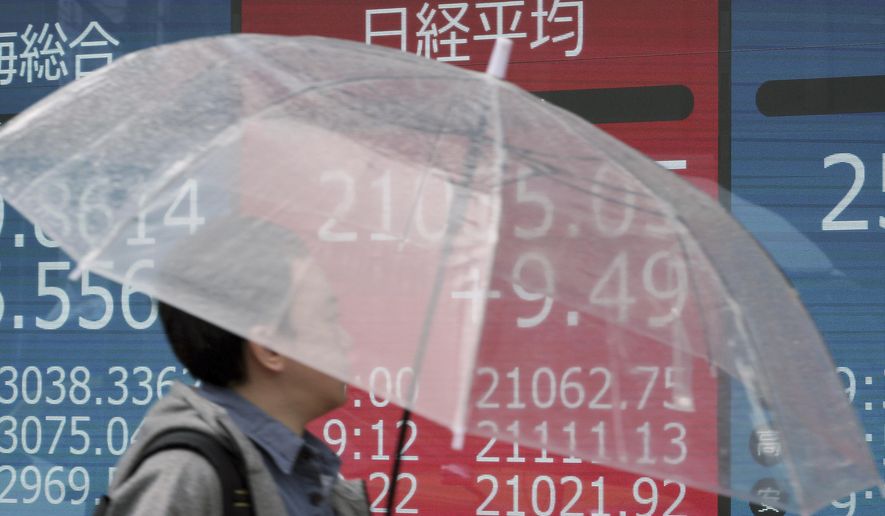 A man with an umbrella looks at an electronic stock board showing Japan's Nikkei 225 index at a securities firm in Tokyo Monday, March 11, 2019. Shares were mixed in Asia on Monday as investors awaited further developments in trade talks between the U.S. and China. (AP Photo/Eugene Hoshiko)