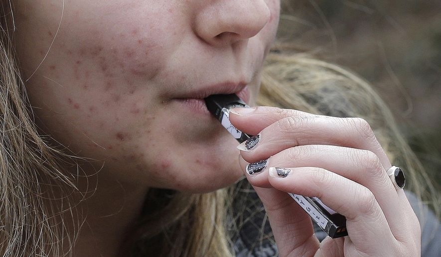 FILE - In this April 11, 2018, file photo, a high school student uses a vaping device near a school campus in Cambridge, Mass. U.S. health regulators are moving ahead with a plan to keep e-cigarettes out of the hands of teenagers by restricting sales of most flavored products in convenience stores and online. (AP Photo/Steven Senne, File) **FILE**