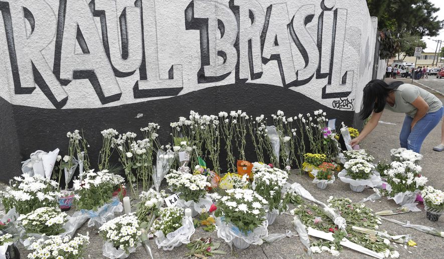 A woman leaves flowers one day after a mass, school shooting outside the Raul Brasil state school in Suzano, Brazil, Thursday, March 14, 2019. Classmates, friends and families began saying goodbye on Thursday, with thousands attending a wake in the Sao Paulo suburb while authorities worked to understand what drove two former students to attack the Raul Brasil State School with a gun, crossbows and small axes. (AP Photo/Andre Penner)