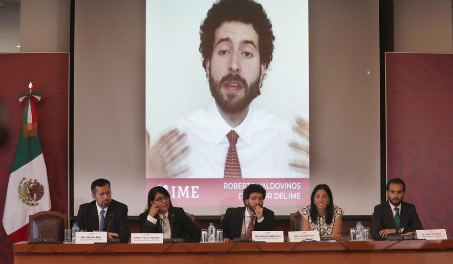 Roberto Valdovinos, head of the Institute for Mexicans Abroad, is shown speaking in a video behind as he gives a news conference, sitting center, in Mexico City, Thursday, March 14, 2019. The Mexican government is launching open-ended public consultation forums in the U.S. to give Mexicans living there a chance to opine on Mexico's national development plan. (AP Photo/Marco Ugarte)