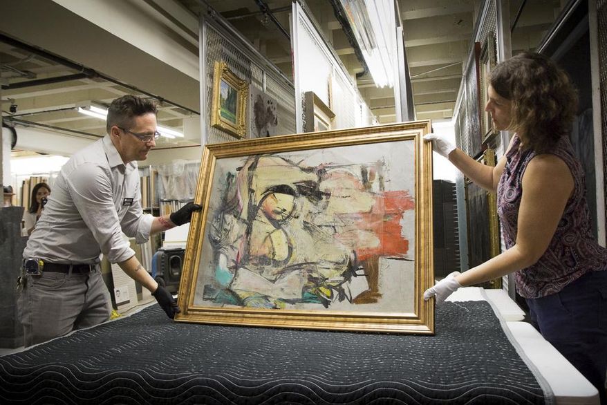 This August 2017 photo shows "Woman-Ochre," a painting by Willem de Kooning, being readied for examination by University of Arizona Museum of Art staff Nathan Saxton, left, and Kristen Schmidt in Tucson, Ariz. More than 30 years after it was stolen from the museum, the recovered painting will be on display back where it all began. (Robert Demers/University of Arizona Communications via AP)