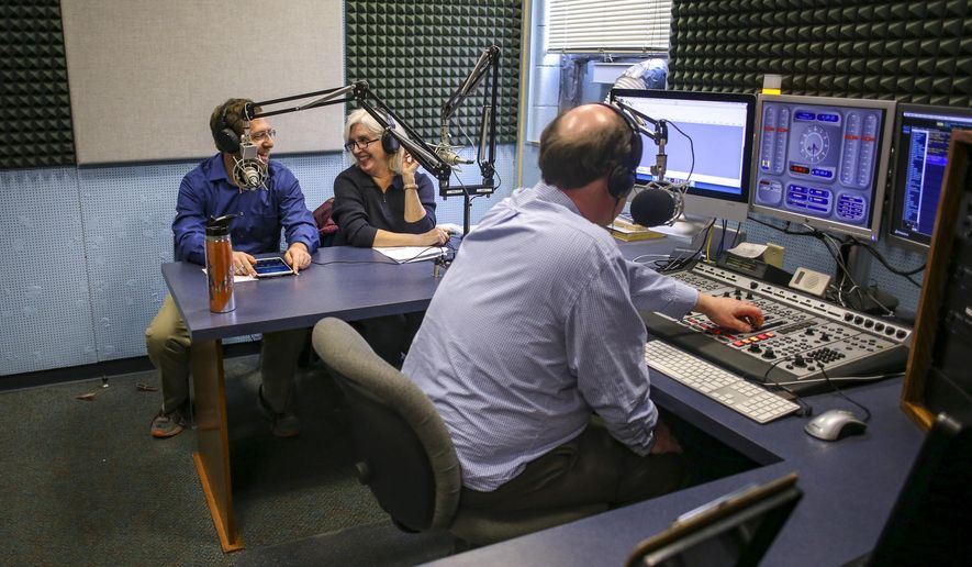 In a Thursday, Feb. 21, 2019 photo, co-hosts Brett Monnard, left, and Terri Toppler smile at one another as station manager David Baker adjusts levels during a recording of "Relevant or Irrelevant" at St.Ambrose University in Davenport,Iowa.  (Andy Abeyta/Quad City Times via AP)