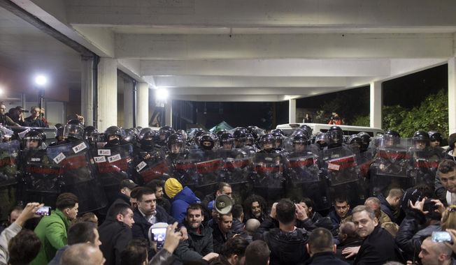 Protesters sit in front of a riot police cordon at an entrance to the state-run TV headquarters in Belgrade, Serbia, Saturday, March 16, 2019. Demonstrators protesting the autocratic rule of Serbian President Aleksandar Vucic burst into the state-run TV headquarters in Belgrade on Saturday to denounce a broadcaster whose reporting they consider highly biased. (AP Photo/Marko Drobnjakovic)