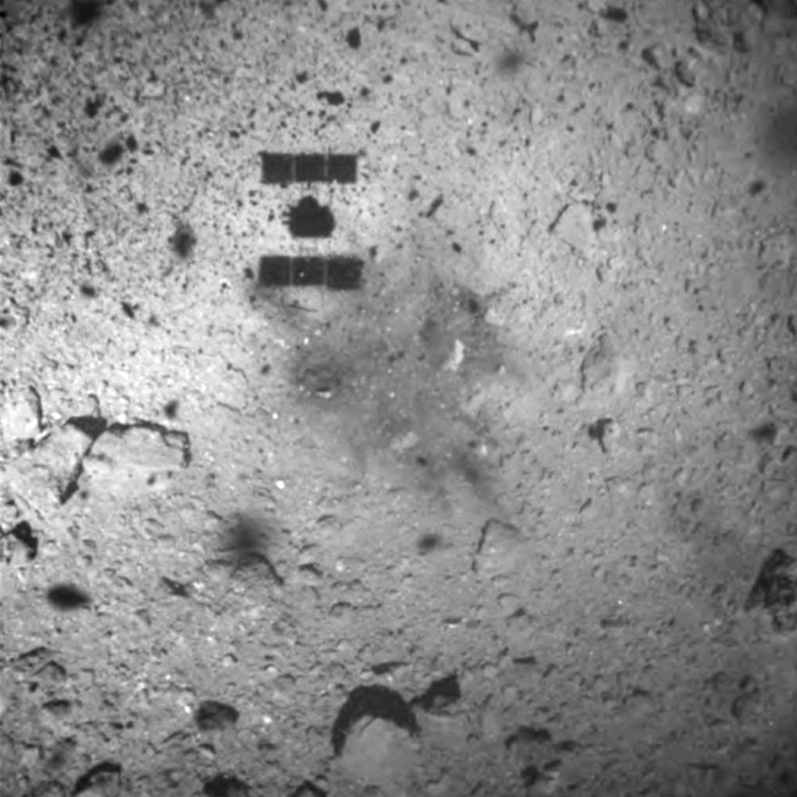 FILE - In this Feb. 22, 2019, file photo, this image released by the Japan Aerospace Exploration Agency (JAXA) shows the shadow, center above, of the Hayabusa2 spacecraft after its successful touchdown on the asteroid Ryugu. Japan's space agency says its Hayabusa2 spacecraft will follow up last month's touchdown on a distant asteroid with another risky mission — to drop an explosive to make a crater and collect underground samples to get possible clues to the origin of the solar system. (JAXA via AP, File)