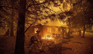 FILE - In this Nov. 9, 2018, file photo firefighters work to keep flames from spreading through the Shadowbrook apartment complex as a wildfire burns through Paradise, Calif. California is calling in the National Guard for the first time to help protect communities from wildfires like the one that destroyed much of the city of Paradise last fall. Starting in April 2019, 110 California National Guard troops will receive 11 days of training in using shovels, rakes and chain saws to thin trees and brush.  (AP Photo/Noah Berger, File)