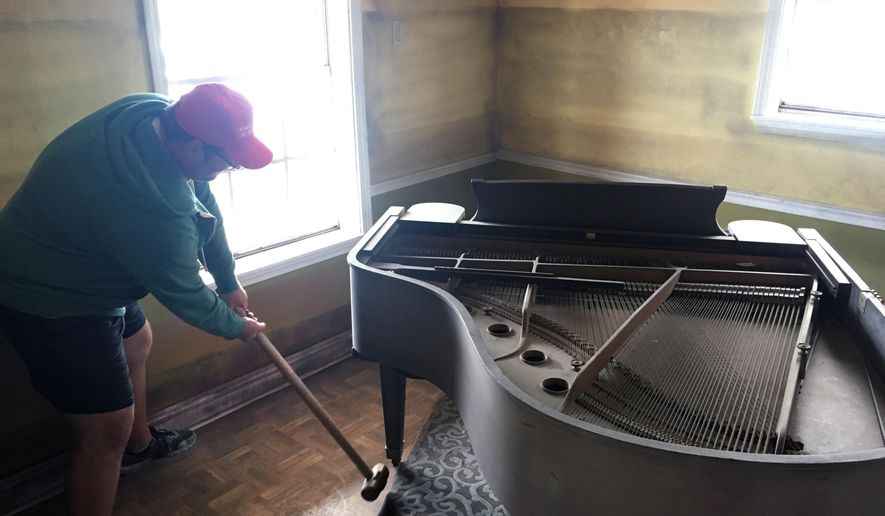 In this Feb. 26, 2019 photo, artist Aaron Angelo takes a sledgehammer to the leg of a baby grand piano in a house where two rooms are being transformed to look as they might have looked once floodwaters receded following Hurricane Katrina in New Orleans. The house sits in front of one of the flood walls that failed when Katrina hit nearly 14 years ago. The nonprofit group Levees.org bought the house and is transforming it as part of its effort to educate the public on the causes of the 2005 flood. (AP Photo/Kevin McGill)