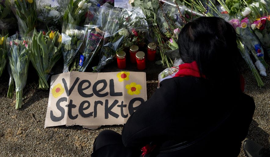 A sign reads "Lots of Strength" as a mourner lays flowers at a makeshift memorial for victims of a shooting incident in a tram in Utrecht, Netherlands, Tuesday, March 19, 2019. A gunman killed three people and wounded others on a tram in the central Dutch city of Utrecht Monday March 18, 2019. (AP Photo/Peter Dejong)