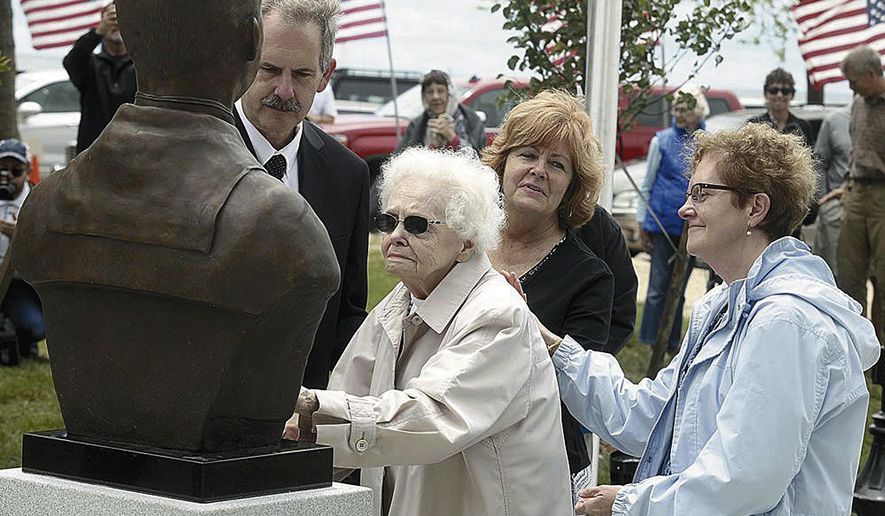 CORRECTS DATE - In this 2017 photo, Peg Ezdebski, surrounded by her children, looks at a bronze bust of her brother and Medal of Honor winner, William Charette, that was placed in the Veterans Memorial in Stearns Park, in Ludington, Mich. (Jeff Kiessel/Ludington Daily News via AP)