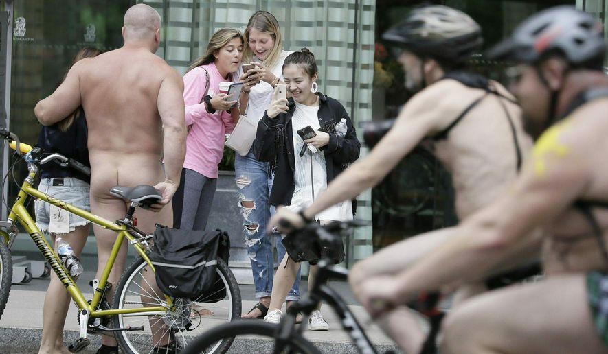 FILE - In this Sept. 8, 2018 file photo, a naked bicyclist poses for photos as other participants ride past during the Philly Naked Bike Ride in Philadelphia. Naked bicyclists say they were so cold riding around Philadelphia last September that this year they’ll do it in August. Organizers of the annual Philly Naked Bike Ride say they’ve “ridden in chilly weather” the last two Septembers so this time they’ll saddle up Aug. 24 and “hope it’s a scorcher!” The nude ride was on Sept. 8 last year and Sept. 9 the year before that, with temperatures reaching only about 70 degrees Fahrenheit. (Elizabeth Robertson/The Philadelphia Inquirer via AP, File)