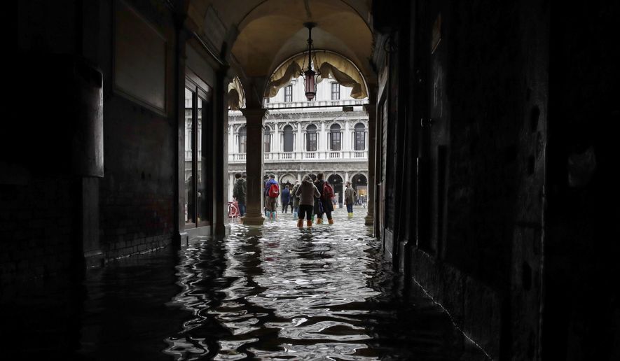 FILE - In this Thursday, Nov. 1, 2018 file photo, tourists walk in the flooded St. Mark's Square in Venice, Italy, as rainstorms and strong winds hit the area. On Thursday, March 28, 2019, the United Nations’ weather agency says extreme weather in 2018 hit 62 million people worldwide last year and created 2 million refugees as man-made climate change worsened. (AP Photo/Luca Bruno)