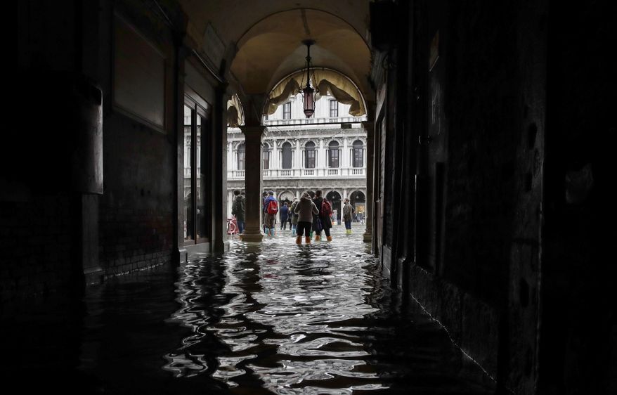 FILE - In this Thursday, Nov. 1, 2018 file photo, tourists walk in the flooded St. Mark's Square in Venice, Italy, as rainstorms and strong winds hit the area. On Thursday, March 28, 2019, the United Nations’ weather agency says extreme weather in 2018 hit 62 million people worldwide last year and created 2 million refugees as man-made climate change worsened. (AP Photo/Luca Bruno)