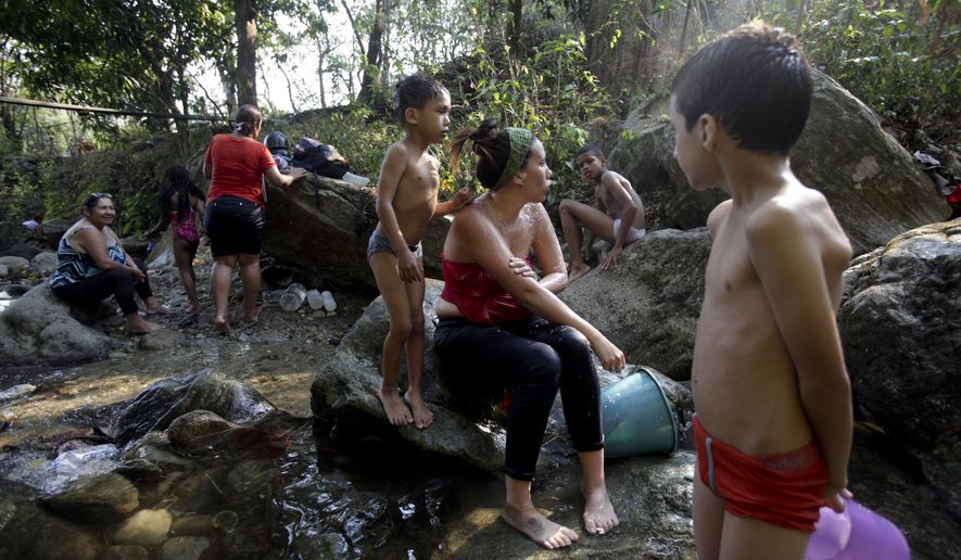 People bathe at a brook in Caracas, Venezuela, Wednesday, March 27, 2019. After days of intermittent electricity supply in Venezuela, which affects the water supply, the people in the capital city have started to collect water from waterfalls and wells and carry it to their homes. (AP Photo/Boris Vergara)