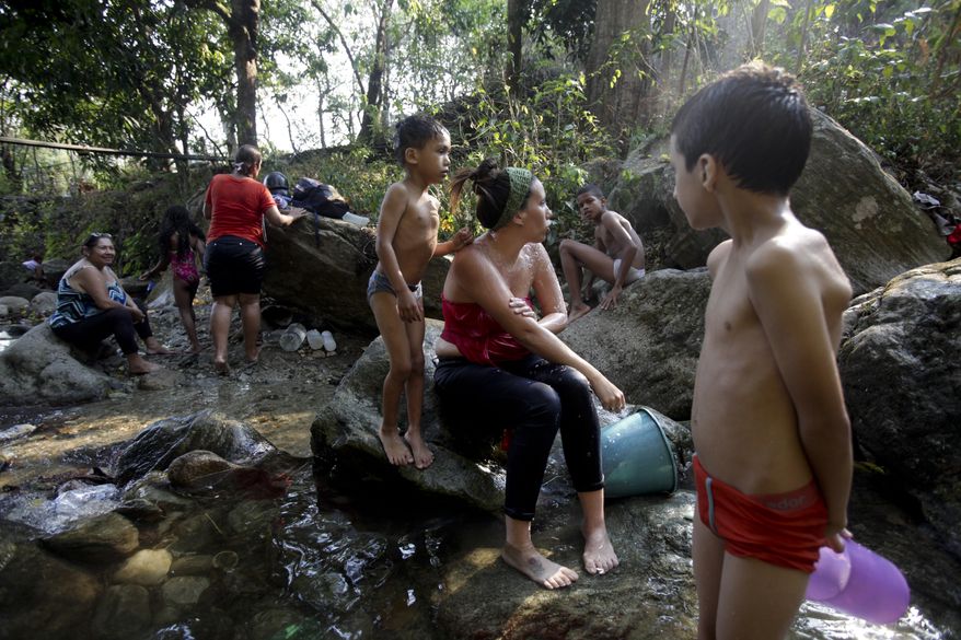 People bathe at a brook in Caracas, Venezuela, Wednesday, March 27, 2019. After days of intermittent electricity supply in Venezuela, which affects the water supply, the people in the capital city have started to collect water from waterfalls and wells and carry it to their homes. (AP Photo/Boris Vergara)