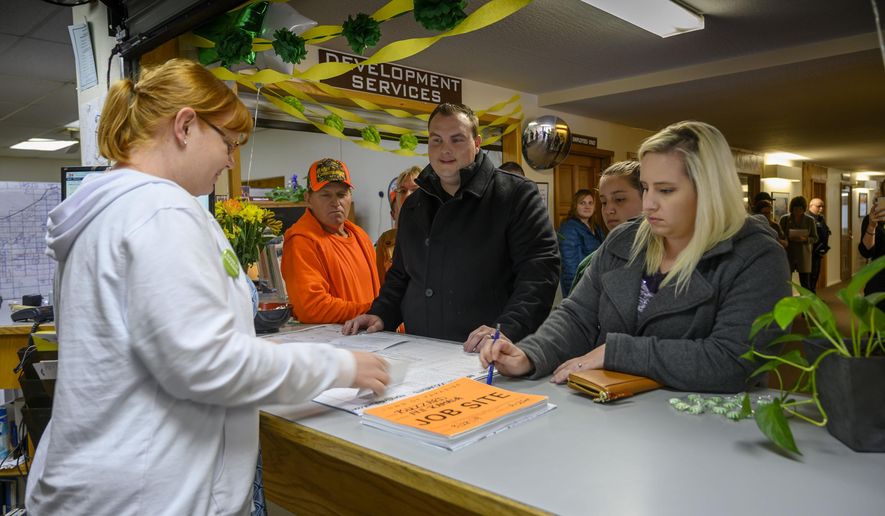 In this photo taken Thursday, March 28, 2019, Anne Vierra,with the town of Paradise, takes payment for the first building permit since the Camp Fire as Jason and Meagann Buzzard plan to rebuild their home in Paradise, Calif. Small signs of rebuilding a Northern California town destroyed by wildfire are sprouting this spring, including the issuing of the first permit to rebuild one of the 11,000 homes destroyed in Paradise five months ago. A city hall clerk on Thursday issued the couple a building permit to replace their home destroyed by the Nov. 8 fire that killed 85 people. The couple told reporters they never thought about leaving. Paradise Mayor Jody Jones said the Buzzards' permit is a sign that the town will rebuild.(Hector Amezcua/The Sacramento Bee via AP)