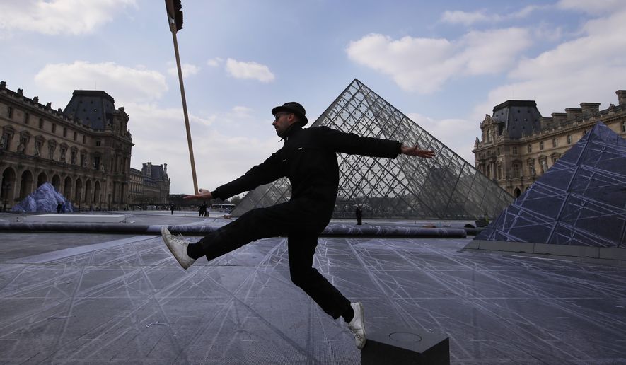 French street artist JR poses in the courtyard of the Louvre Museum near the glass pyramid designed by architect Leoh Ming Pei, in Paris, Wednesday, March 27, 2019 as the Louvre Museum celebrates the 30th anniversary of its glass pyramid. JR project is a giant collage of the pyramid to bring it out of the ground by revealing the foundations of the Napoleon courtyard where it is erected. (AP Photo/Francois Mori)