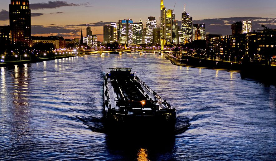 A cargo vessel passes along the river Main, with buildings of the banking district in background, in Frankfurt, Germany, as the sun sets Monday, March 18, 2019. (AP Photo/Michael Probst)
