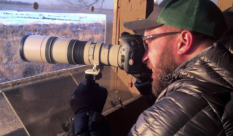 In this Thursday, March 28, 2019 photo, Morgan Dowdall , of Loveland, Colo., sets up his camera to catch a sandhill crane in action while on a guided tour at the Crane Trust Nature and Visitors Center south of Alda, Neb. The numbers were low on this visit because of the weather, and there were only about 3,000 cranes on the river instead of the usual 10,000 or more. (Robert Pore/The Independent via AP)